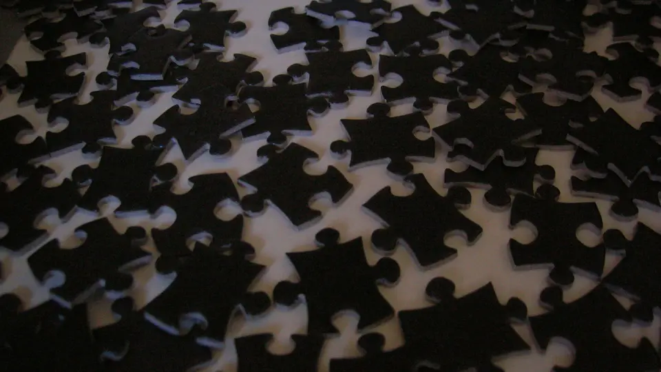 Loose black jigsaw puzzle pieces scattered on a pale table, waiting to be connected