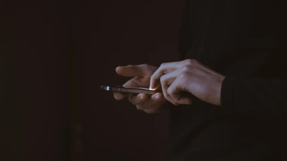 Two hands holding a smartphone against a dark background.