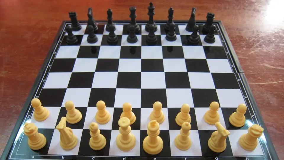 Black and cream chess pieces lined up on a chess board ready to play