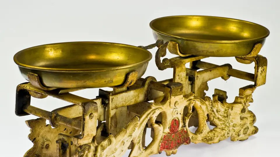An antique brass balance scale with two empty pans on an ornate cast-iron stand, photographed against a white background.
