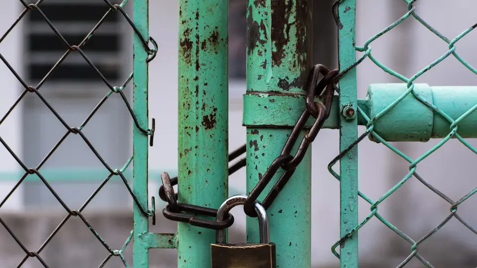 A padlock and rusty chain fastening a green metal gate in a chain-link fence.