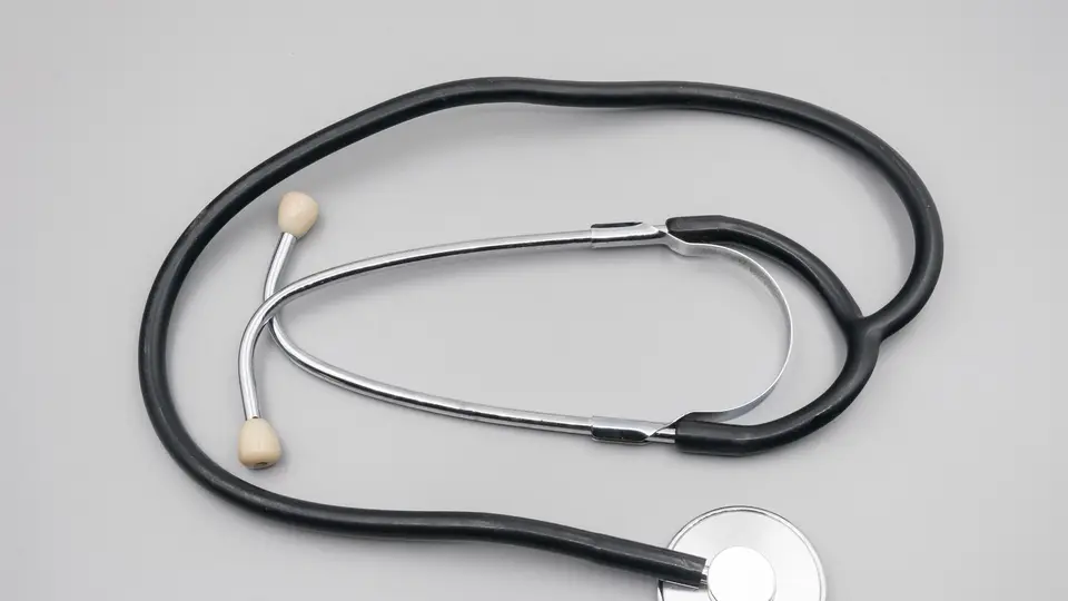 A stethoscope with black tubing and a silver chest piece laid out on a plain light grey surface